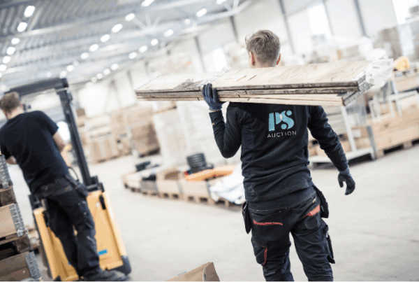 Medarbetare på PS Auction bär utrustning i lagerlokal inför försäljning av begagnade maskiner på auktion.
