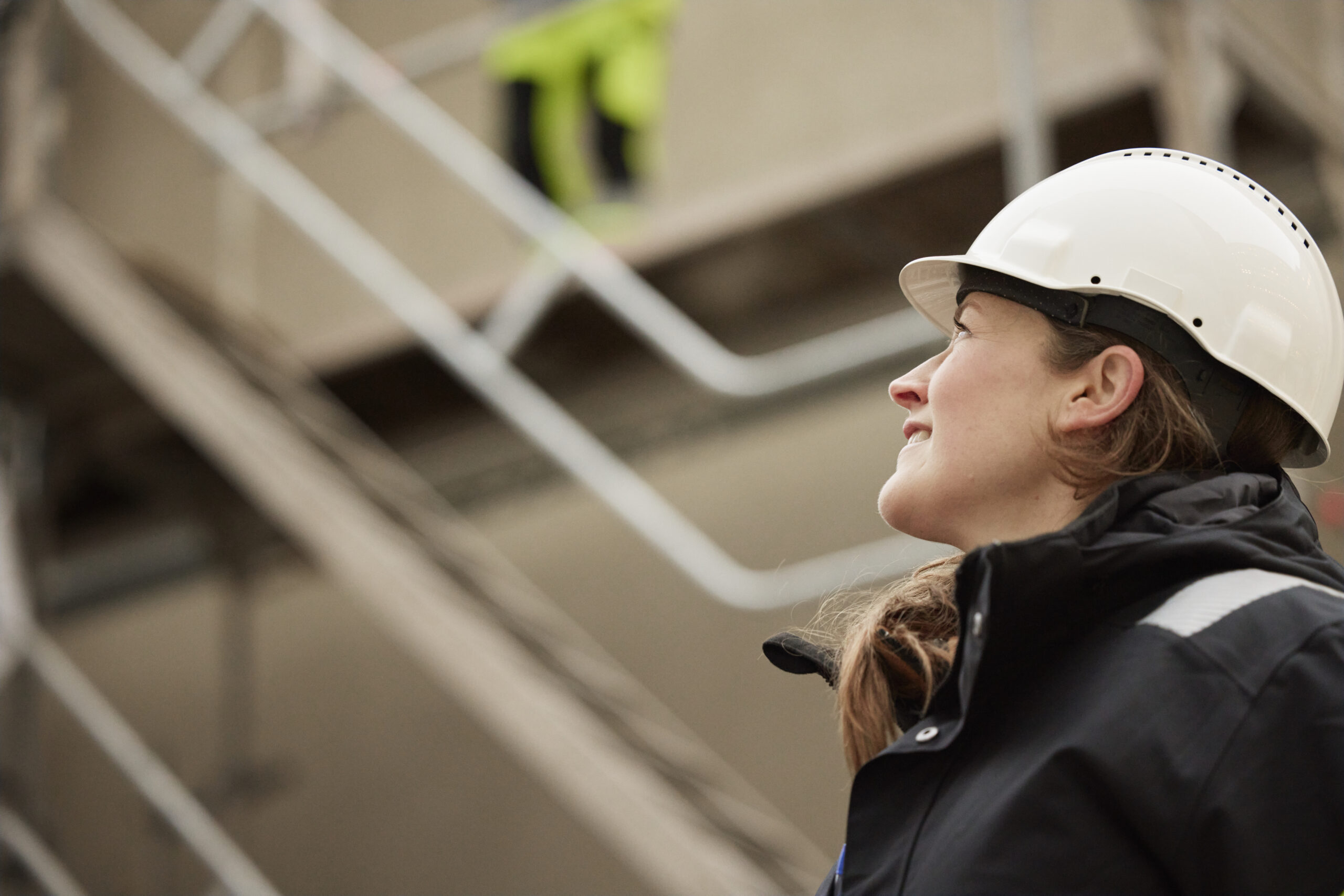 "Kvinna i skyddshjälm i industrimiljö blickar upp – symboliserar det operativa arbetet med att identifiera utrustning som kan återbrukas i cirkulärt inköpsarbete."