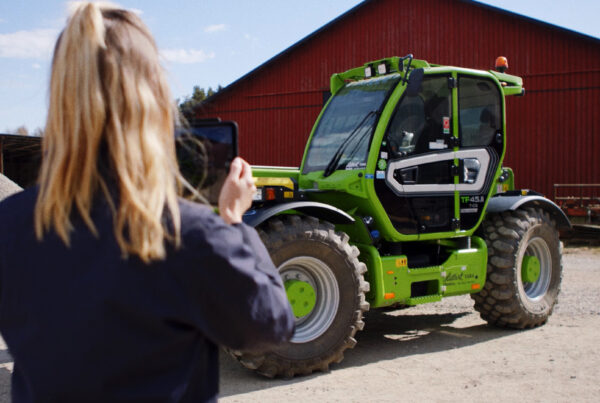Kvinna fotograferar en begagnad grön teleskoplastare inför försäljning via maskinauktion online.