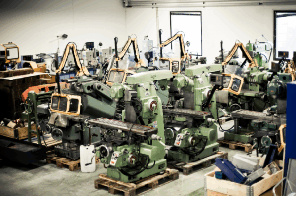 Industrihall med ett flertal begagnade fräsmaskiner och verkstadsutrustning uppställda inför försäljning på auktion.